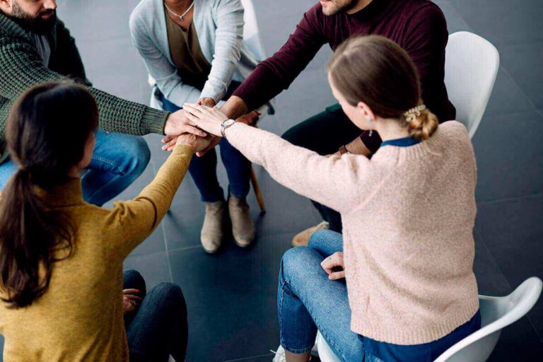 support group people sitting in a circle with their hands in the center